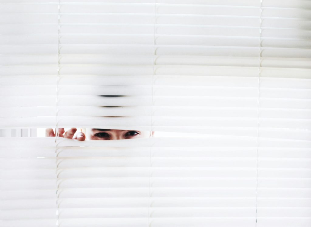 at hear, we take digital privacy very seriously A person peeks through white blinds, creating an intriguing sense of curiosity.